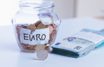 Monety Euro w szklanym słoju i plik banknotów