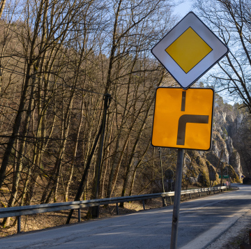 Żółty znak drogowy, zakręt i droga z pierwszeństwem przejazdu.