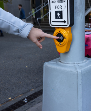 Ręka naciskająca przycisk na sygnalizacji świetlnej przy przejściu dla pieszych - zdjęcie stockowe