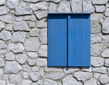 Okno z niebieska okiennicą w ścianie z kamieni