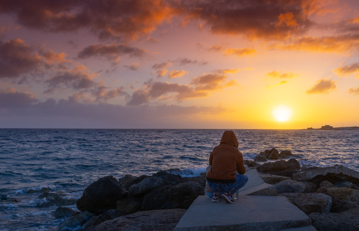 Postać w kapturze i zachód słońca nad morzem